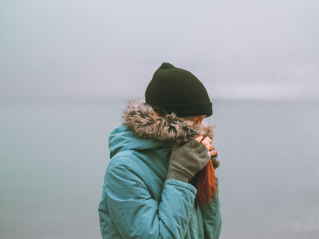 woman in green jacket and black knit cap covering her face with her hand