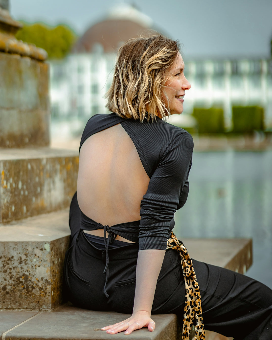 A woman with blonde hair in a black backless top sitting on stone steps