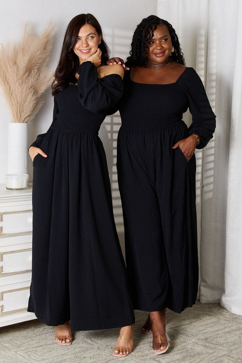 Two women in black off-shoulder maxi dresses posing indoors.